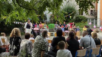 Foto zeigt: Die Schulleiterin in ihrer Ansprache anlässlich der Einschulung. Hinter  ihr befinden sich Kinder und Pädagogen der Musik- und Tanzgruppe.